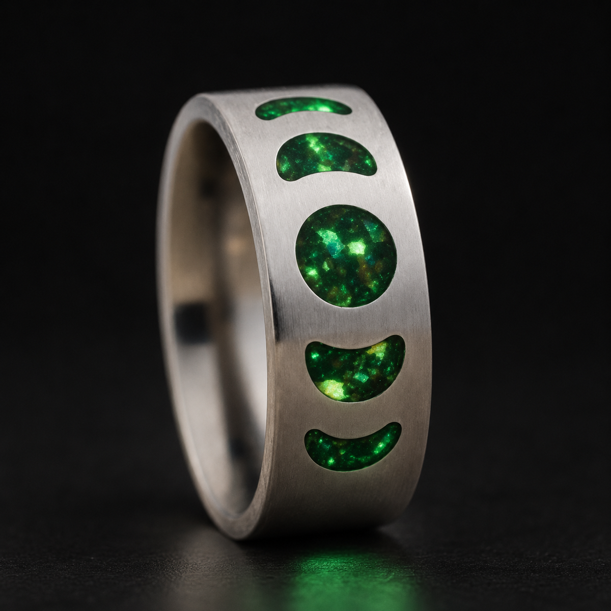 Moon Phase Vulcan handcrafted titanium ring with green glowing moon phase inlays on a dark background